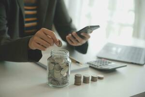 saving money and accounting concept. business man putting coin insert to jar and make acounting book for finance management to investment and saving. photo