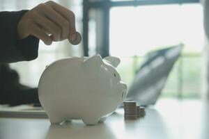 saving money and accounting concept. business man putting coin insert to jar and make acounting book for finance management to investment and saving. photo