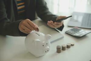 saving money and accounting concept. business man putting coin insert to jar and make acounting book for finance management to investment and saving. photo