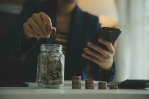 saving money and accounting concept. business man putting coin insert to jar and make acounting book for finance management to investment and saving. photo