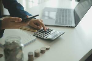 saving money and accounting concept. business man putting coin insert to jar and make acounting book for finance management to investment and saving. photo