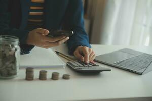 ahorro dinero y contabilidad concepto. negocio hombre poniendo moneda insertar a tarro y hacer contabilidad libro para Finanzas administración a inversión y ahorro. foto