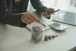 saving money and accounting concept. business man putting coin insert to jar and make acounting book for finance management to investment and saving. photo