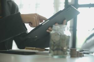 ahorro dinero y contabilidad concepto. negocio hombre poniendo moneda insertar a tarro y hacer contabilidad libro para Finanzas administración a inversión y ahorro. foto