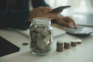 saving money and accounting concept. business man putting coin insert to jar and make acounting book for finance management to investment and saving. photo