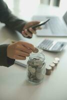 saving money and accounting concept. business man putting coin insert to jar and make acounting book for finance management to investment and saving. photo