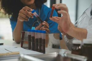 Medical worker in lab coat and sterile mask, doing a microscope analysis while her colleague are working behind photo