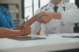 Doctor and patient shaking hands in the office, they are sitting at desk, hands close up photo