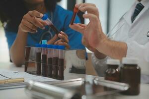 Medical worker in lab coat and sterile mask, doing a microscope analysis while her colleague are working behind photo