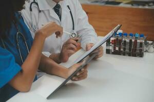 Medical worker in lab coat and sterile mask, doing a microscope analysis while her colleague are working behind photo