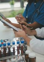 Medical worker in lab coat and sterile mask, doing a microscope analysis while her colleague are working behind photo