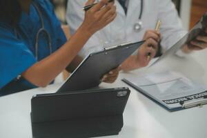 Focused mature male doctor and female nurse look at tablet screen discuss anamnesis together. Concentrated diverse medical professionals use pad device, engaged in team thinking in hospital. photo