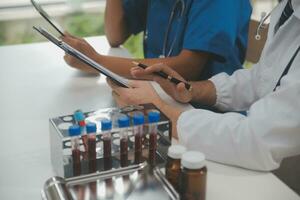Medical worker in lab coat and sterile mask, doing a microscope analysis while her colleague are working behind photo