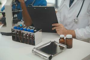 Medical worker in lab coat and sterile mask, doing a microscope analysis while her colleague are working behind photo