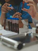 Medical worker in lab coat and sterile mask, doing a microscope analysis while her colleague are working behind photo