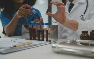 Medical worker in lab coat and sterile mask, doing a microscope analysis while her colleague are working behind photo