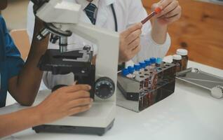 Medical worker in lab coat and sterile mask, doing a microscope analysis while her colleague are working behind photo