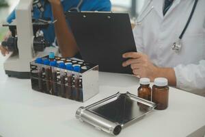 Medical worker in lab coat and sterile mask, doing a microscope analysis while her colleague are working behind photo