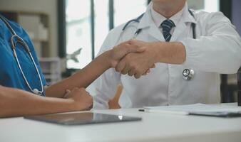 Doctor and patient shaking hands in the office, they are sitting at desk, hands close up photo