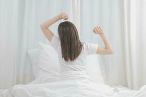 eficiente joven milenario niña sentado en un cama en el mañana, usos ordenador portátil computadora y come croissants y bebidas café para desayuno foto