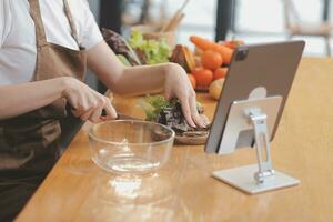 Delicious fruit and vegetables on a table and woman cooking. Housewife is cutting green cucumbers on a wooden board for making fresh salad in the kitchen. photo