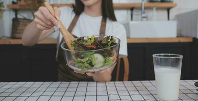 Delicious fruit and vegetables on a table and woman cooking. Housewife is cutting green cucumbers on a wooden board for making fresh salad in the kitchen. photo