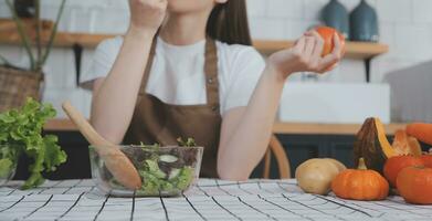 Delicious fruit and vegetables on a table and woman cooking. Housewife is cutting green cucumbers on a wooden board for making fresh salad in the kitchen. photo