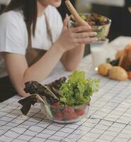 Delicious fruit and vegetables on a table and woman cooking. Housewife is cutting green cucumbers on a wooden board for making fresh salad in the kitchen. photo