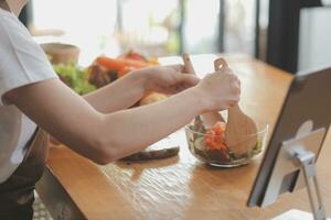 Delicious fruit and vegetables on a table and woman cooking. Housewife is cutting green cucumbers on a wooden board for making fresh salad in the kitchen. photo