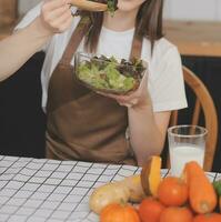 Delicious fruit and vegetables on a table and woman cooking. Housewife is cutting green cucumbers on a wooden board for making fresh salad in the kitchen. photo