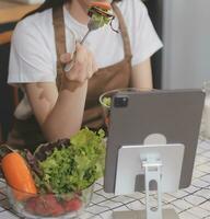 Delicious fruit and vegetables on a table and woman cooking. Housewife is cutting green cucumbers on a wooden board for making fresh salad in the kitchen. photo