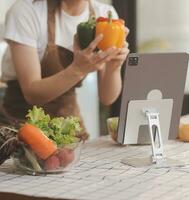 Delicious fruit and vegetables on a table and woman cooking. Housewife is cutting green cucumbers on a wooden board for making fresh salad in the kitchen. photo