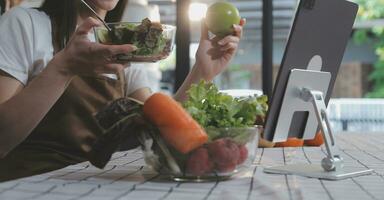 Delicious fruit and vegetables on a table and woman cooking. Housewife is cutting green cucumbers on a wooden board for making fresh salad in the kitchen. photo