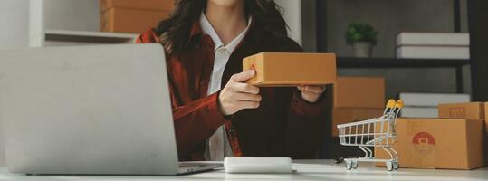 Portrait young attractive hipster asia female owner startup look at camera work happy with box at home prepare parcel delivery in sme supply chain, procurement, omnichannel ecommerce online concept. photo
