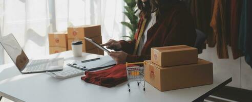 retrato joven atractivo hipster Asia hembra propietario puesta en marcha Mira a cámara trabajo contento con caja a hogar preparar paquete o empaquetar entrega en SME suministro cadena, obtención, omnicanal comercio electrónico en línea concepto. foto