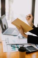Asian Businesswoman Using laptop computer and working at office with calculator document on desk, doing planning analyzing the financial report, business plan investment, finance analysis concept. photo