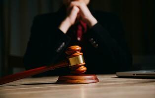 Justice and law concept.Male judge in a courtroom with the gavel, working with, computer and docking keyboard, eyeglasses, on table in morning light photo