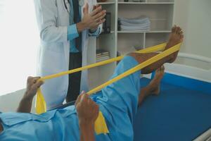 Male patient using elastic band while doing physical exercises for leg muscles at modern clinic, rehabilitation center or hospital. Close up of man's foot. Physiotherapy concept photo