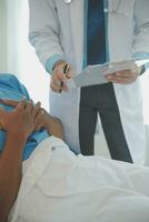 Close up of doctor sitting on bedside of male patient in hospital photo