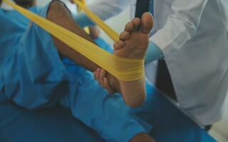Male patient using elastic band while doing physical exercises for leg muscles at modern clinic, rehabilitation center or hospital. Close up of man's foot. Physiotherapy concept photo