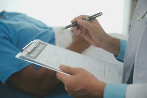 Close up of doctor sitting on bedside of male patient in hospital photo