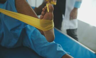 Male patient using elastic band while doing physical exercises for leg muscles at modern clinic, rehabilitation center or hospital. Close up of man's foot. Physiotherapy concept photo