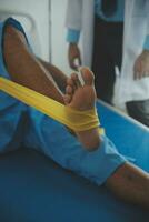 Male patient using elastic band while doing physical exercises for leg muscles at modern clinic, rehabilitation center or hospital. Close up of man's foot. Physiotherapy concept photo