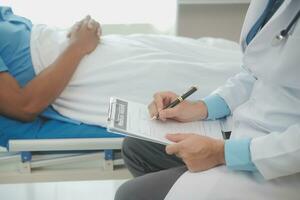 Close up of doctor sitting on bedside of male patient in hospital photo