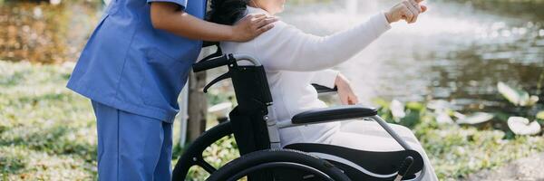 Asian young woman nurse at nursing home take care disabled senior man. Caregiver doctor serve physical therapy for older elderly patient to exercise and practice walking on walker or cane at backyard. photo