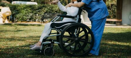 Asian young woman nurse at nursing home take care disabled senior man. Caregiver doctor serve physical therapy for older elderly patient to exercise and practice walking on walker or cane at backyard. photo