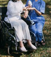 Asian young woman nurse at nursing home take care disabled senior man. Caregiver doctor serve physical therapy for older elderly patient to exercise and practice walking on walker or cane at backyard. photo