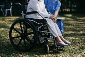 Asian young woman nurse at nursing home take care disabled senior man. Caregiver doctor serve physical therapy for older elderly patient to exercise and practice walking on walker or cane at backyard. photo