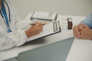 Doctor and patient sitting and talking at medical examination at hospital office, close-up. Therapist filling up medication history records. Medicine and healthcare concept. photo