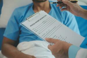 Close up of doctor sitting on bedside of male patient in hospital photo